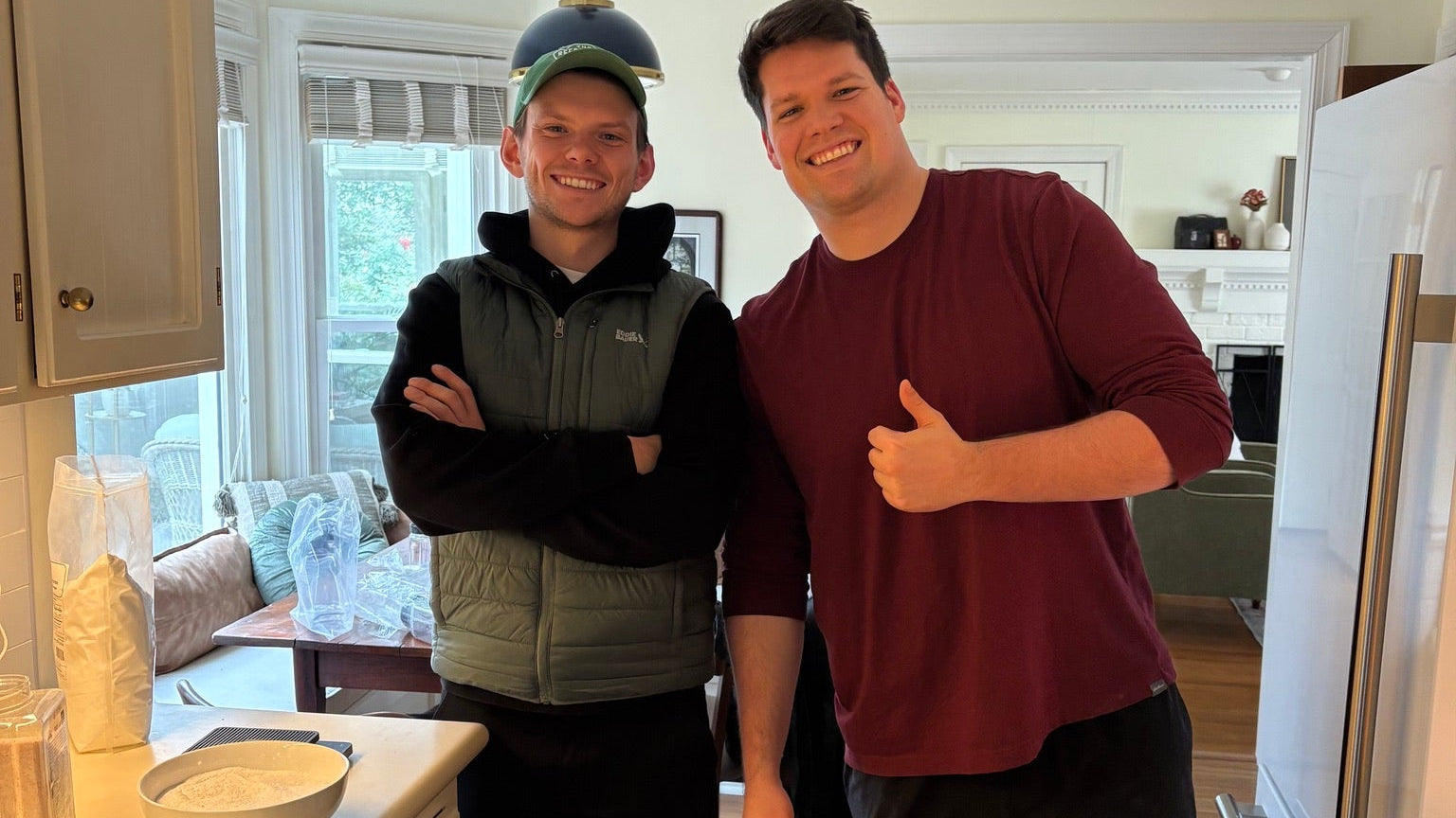 Two people standing in a kitchen, one giving a thumbs-up